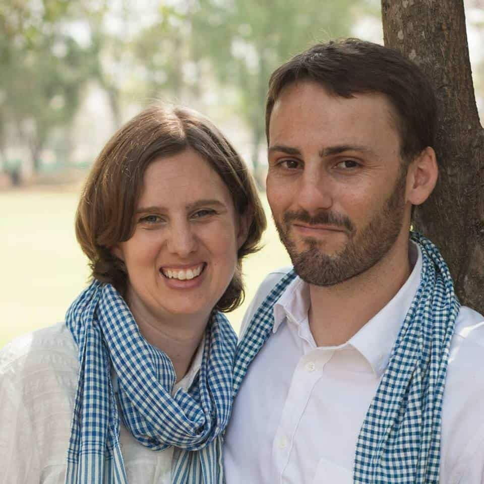 Two volunteers, a smiling woman and a man, both wearing matching checkered scarves, standing together outdoors