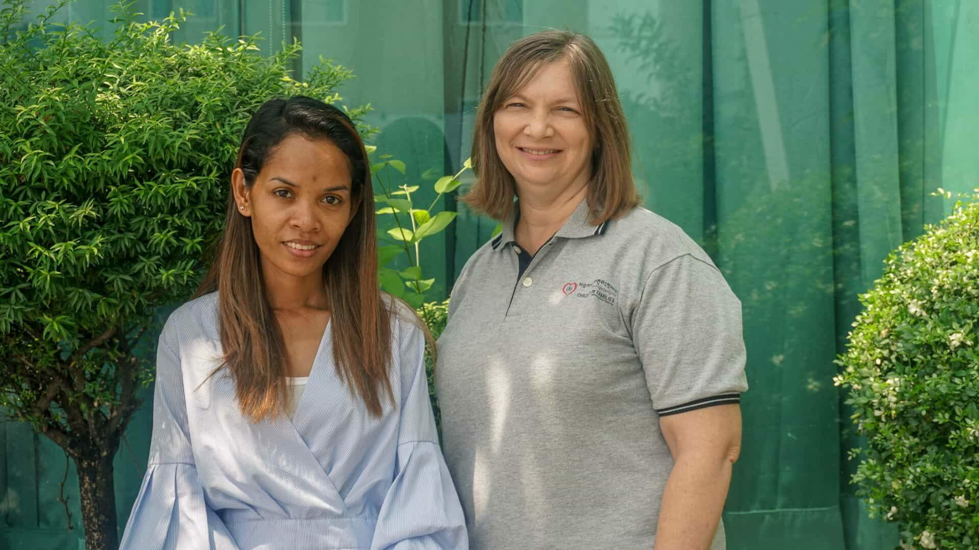 Two women stand smiling side by side outdoors in front of greenery, ahead of ABLE's trip to Geneva