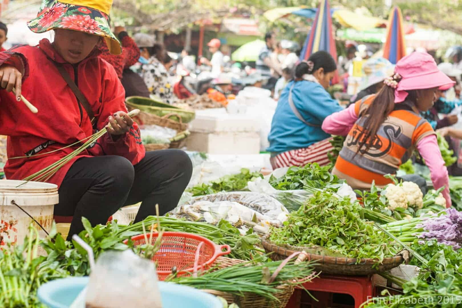 Vendors sell fresh greens and vegetables at a busy outdoor market