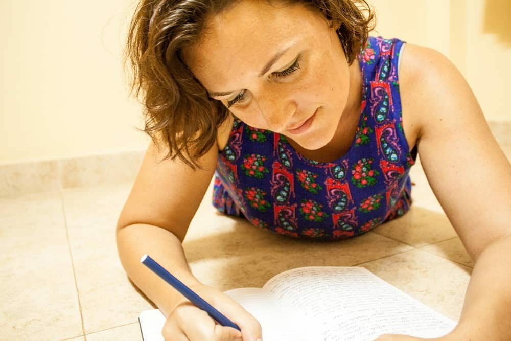 Woman lying on the floor writing in a notebook with a pencil