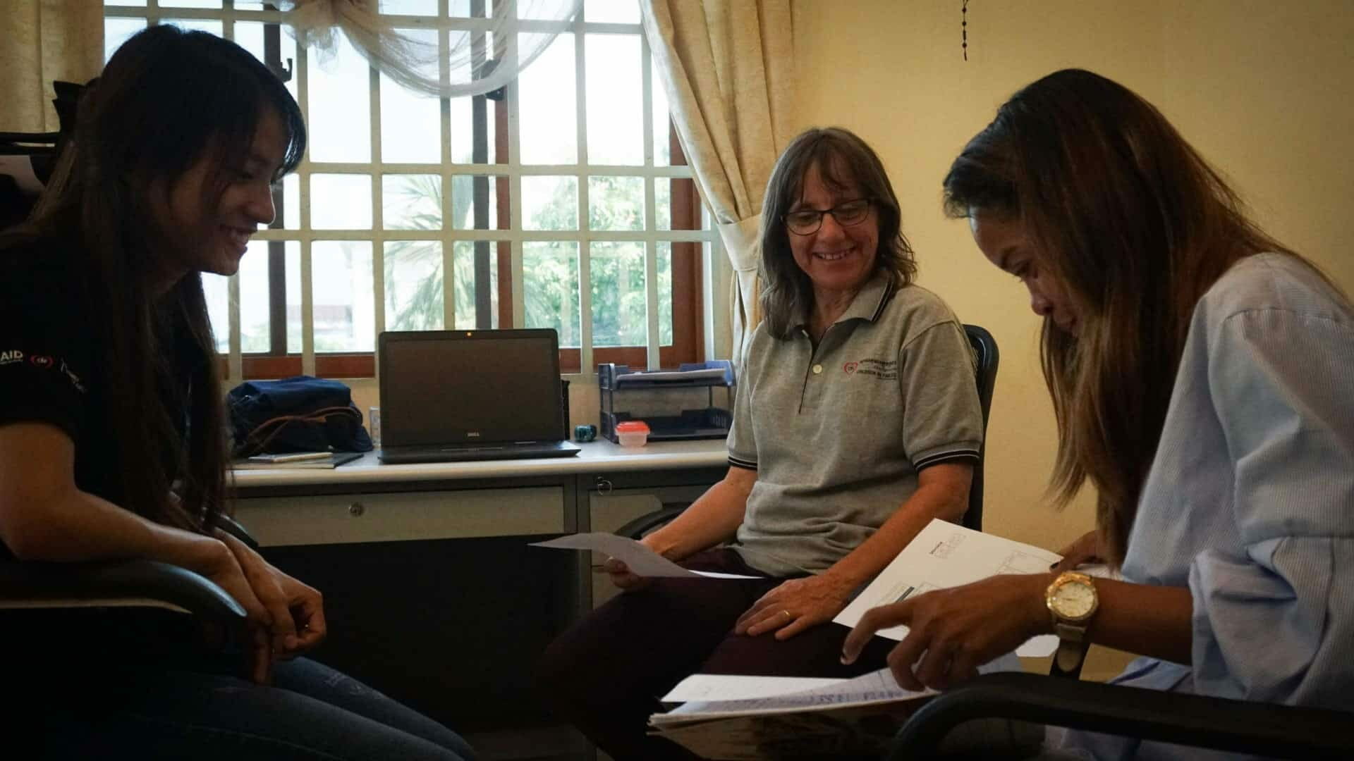 Bridget sits smiling with two ABLE staff reviewing papers together in an office, discussing autism support plans