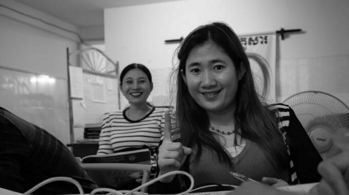 Damy smiles while working at a desk in an office, with a colleague seated behind her