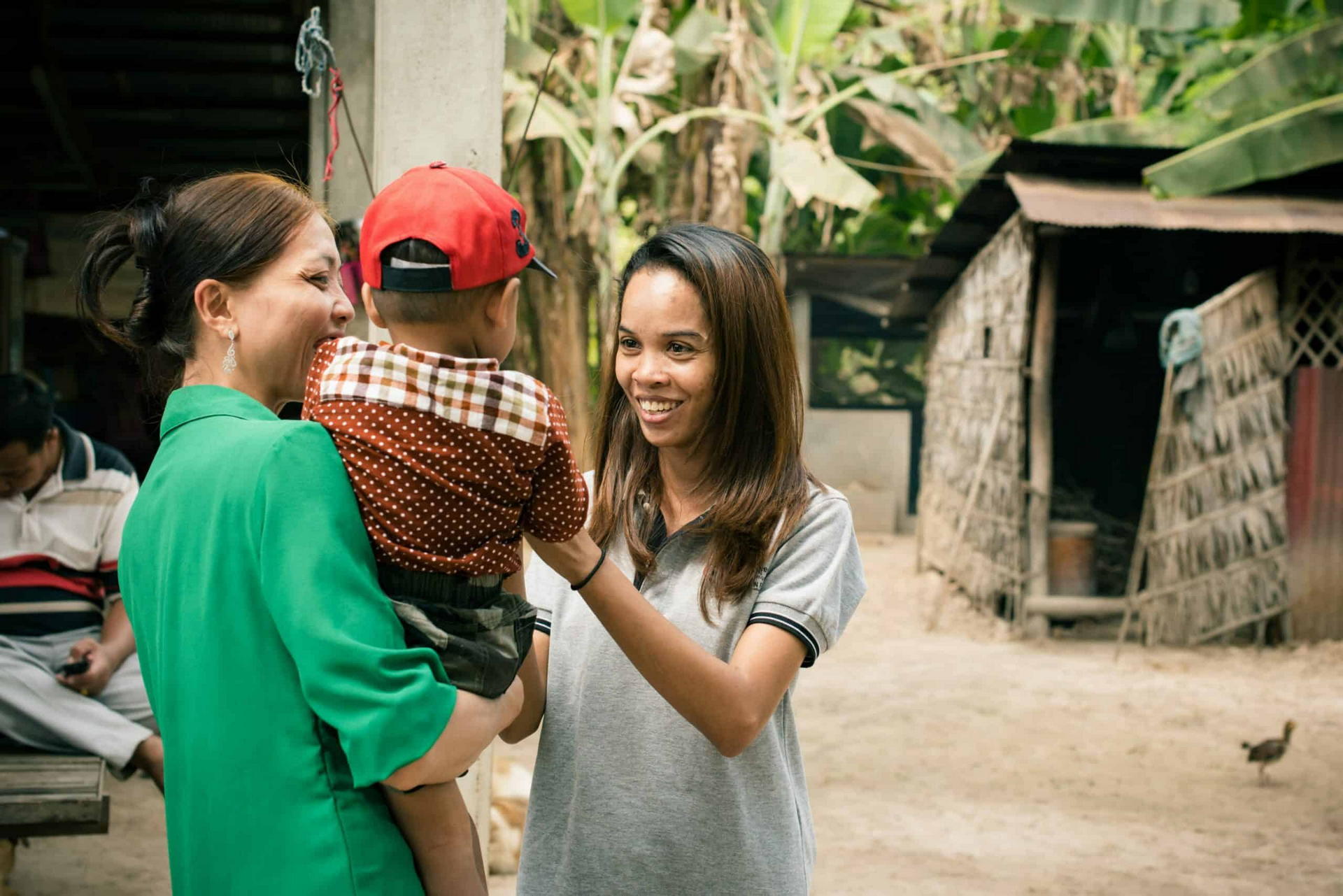 A worker smiles with a mother holding her young son outside their rural home during a home visit