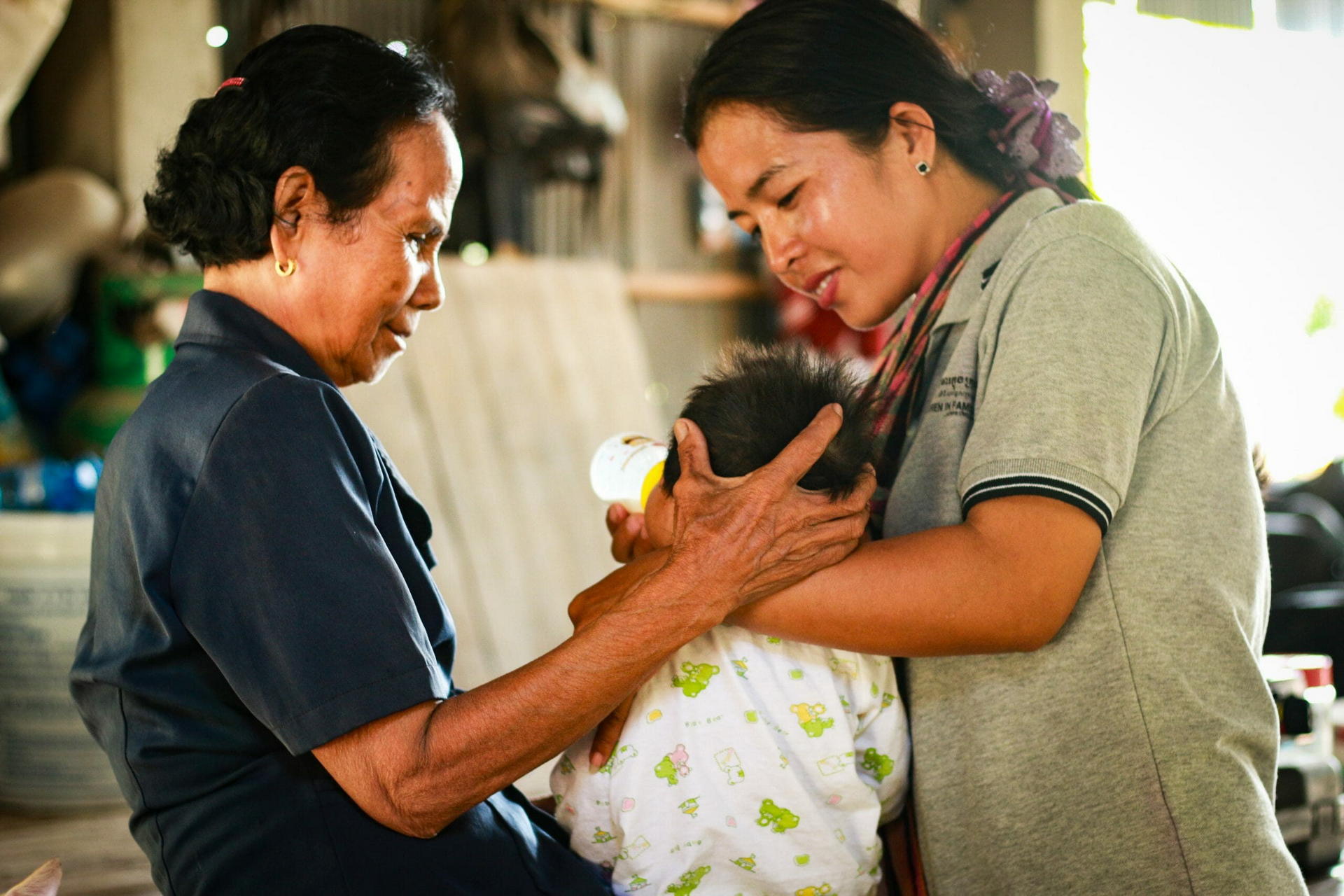A social worker visits a family, gently comforting a young child held by its mother while feeding it from a bottle