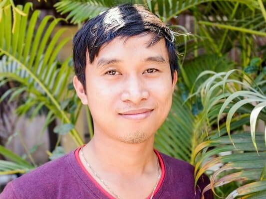 Chantrea, the new Kinship Care Manager, smiling in front of green foliage