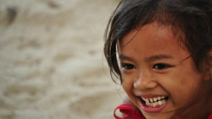 Young girl smiling brightly, close-up view against a rustic wall background