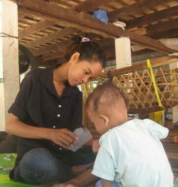 Srey Ny, physiotherapist for ABLE, sits with a young child during a therapy session in an open-air home setting