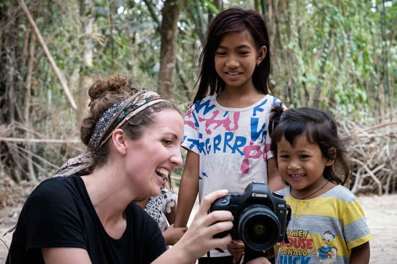 Woman shows two smiling children a photo on her camera in a forested setting