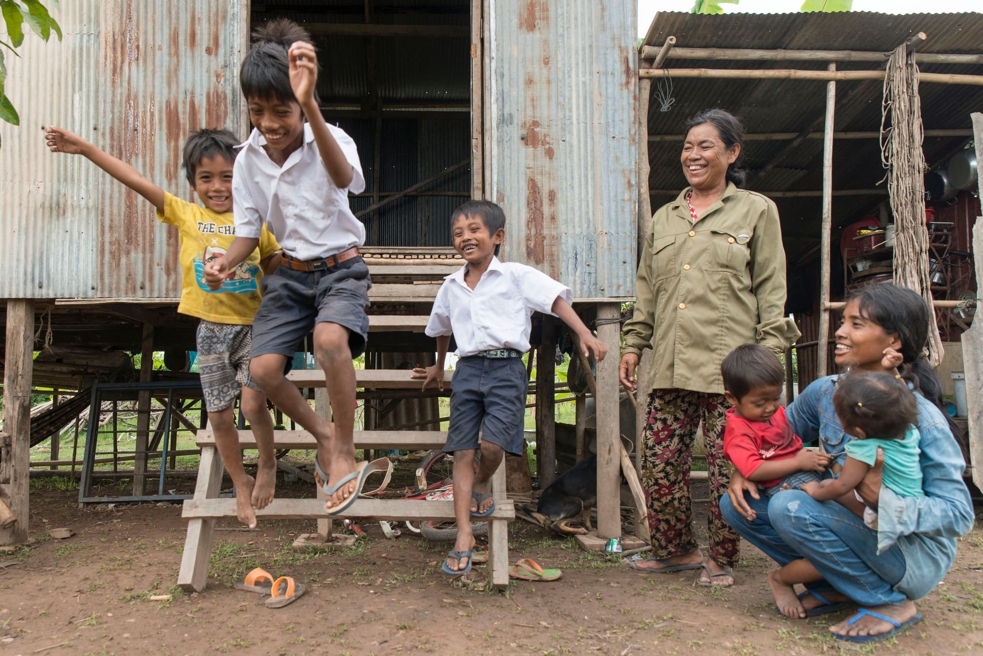 Children joyfully jumping and playing outside a home while family members watch and laugh nearby
